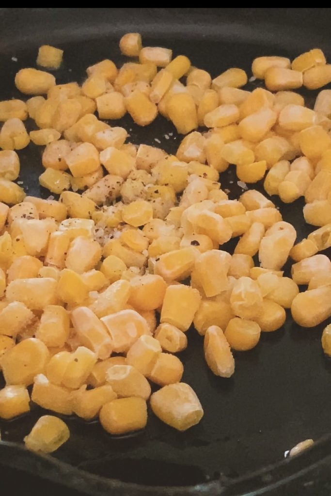 Corn kernels cooking in a cast iron pan.