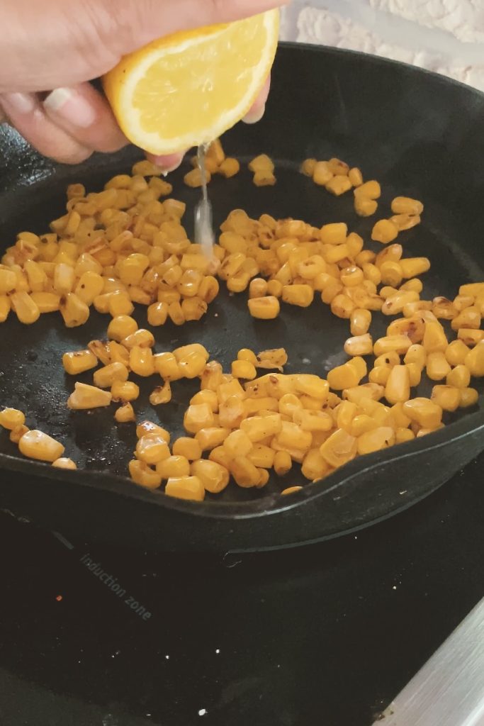Squeezing lemon onto corn kernels cooking in a cast iron pan.