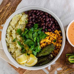 A bowl of mashed potatoes topped with beans, corn, charred jalapenos, cilantro and sauce.