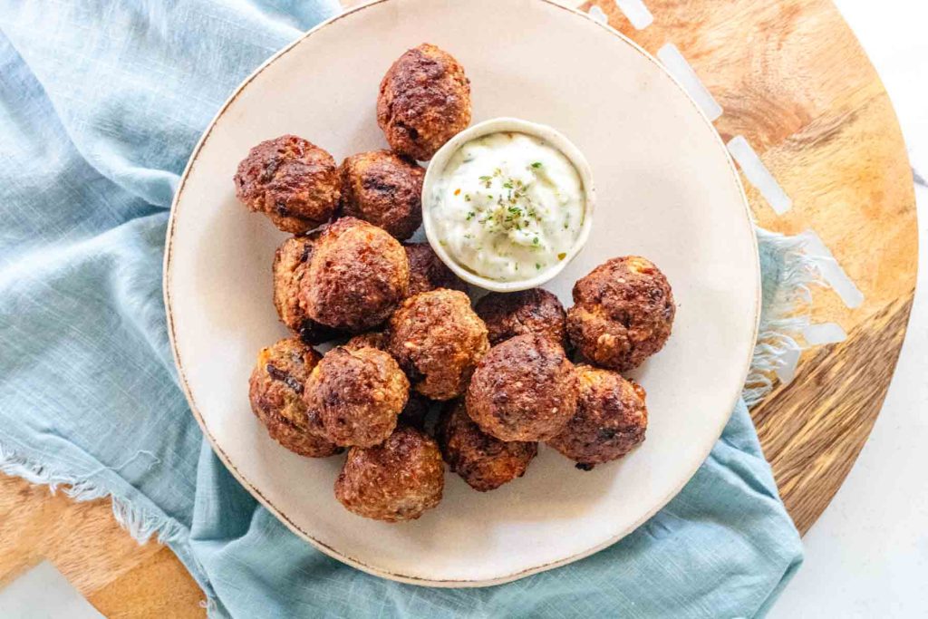 Meatballs on a plate with a bowl of Tzatziki.