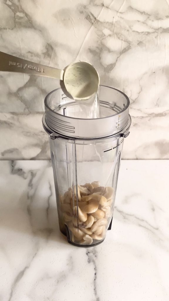 Water is added to a blender cup with cashews in it.