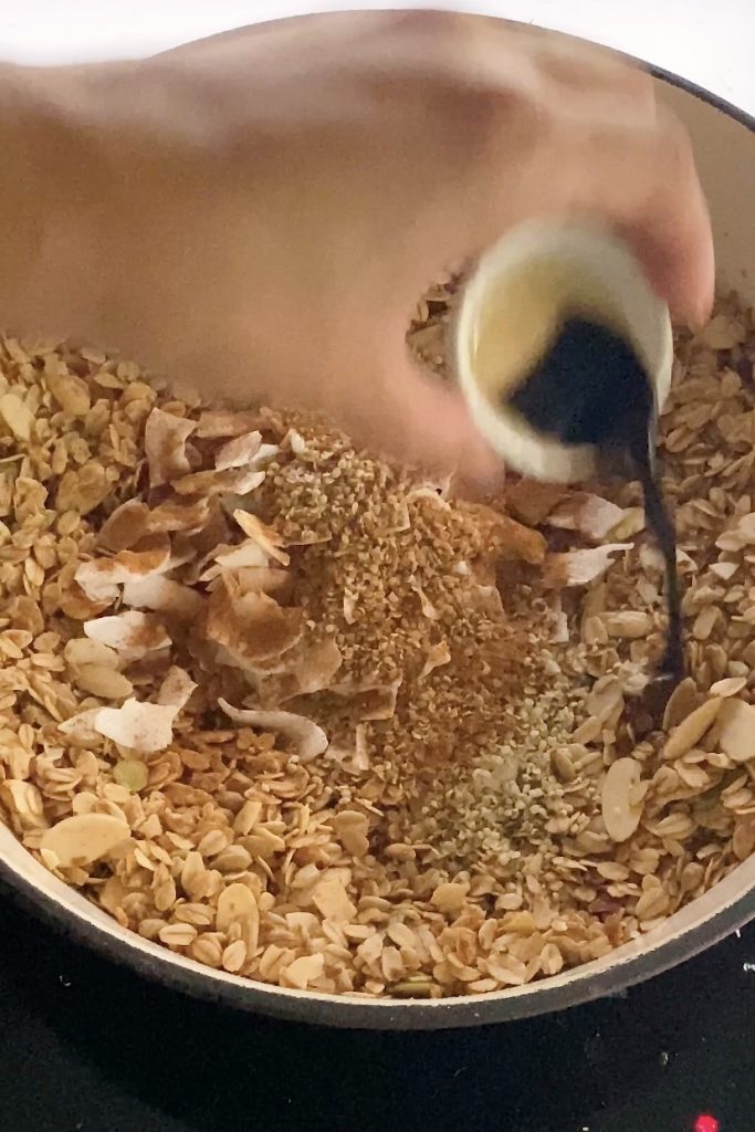 Vanilla extract is poured into granola in a skillet.
