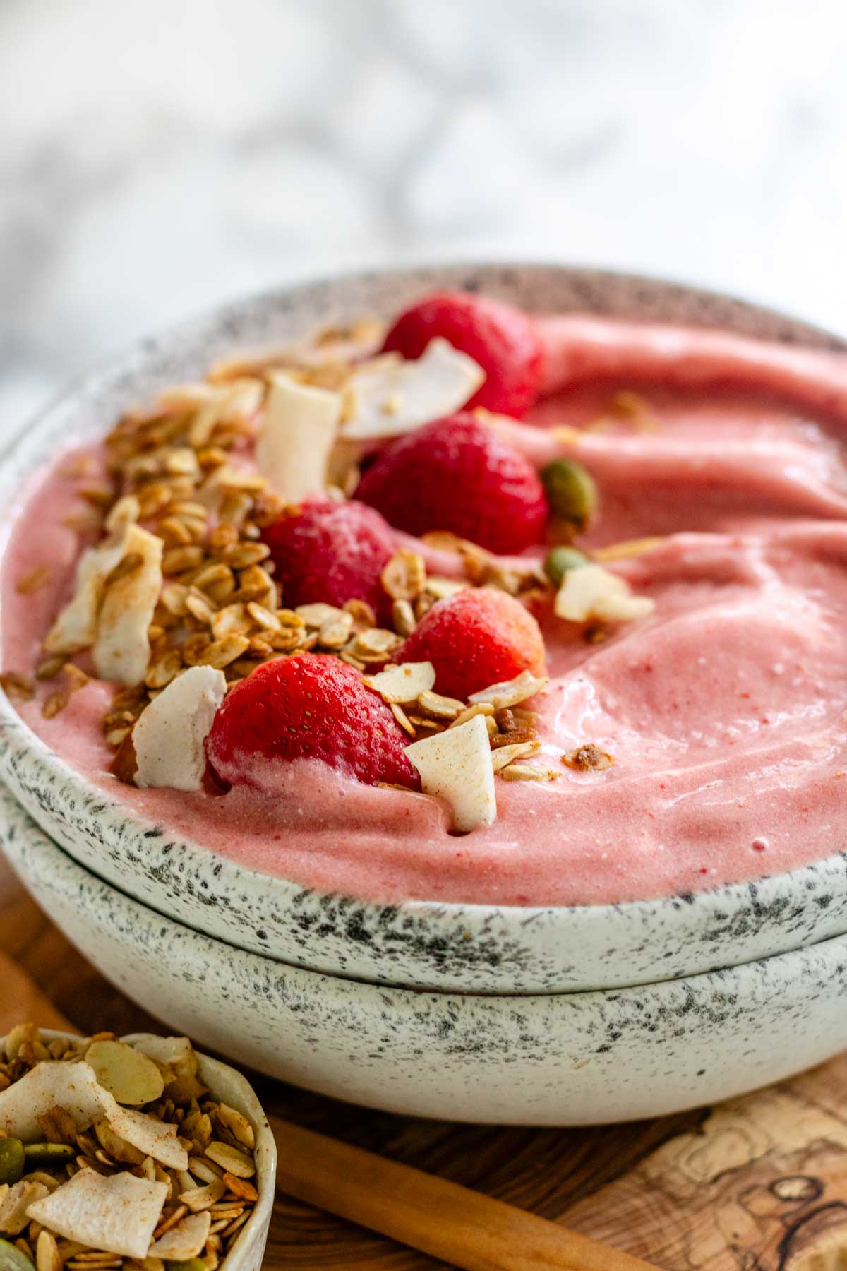 A pink smoothie bowl with strawberries and granola on top.