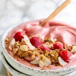 A pink smoothie bowl with strawberries and granola on top with a text title for pinterest.