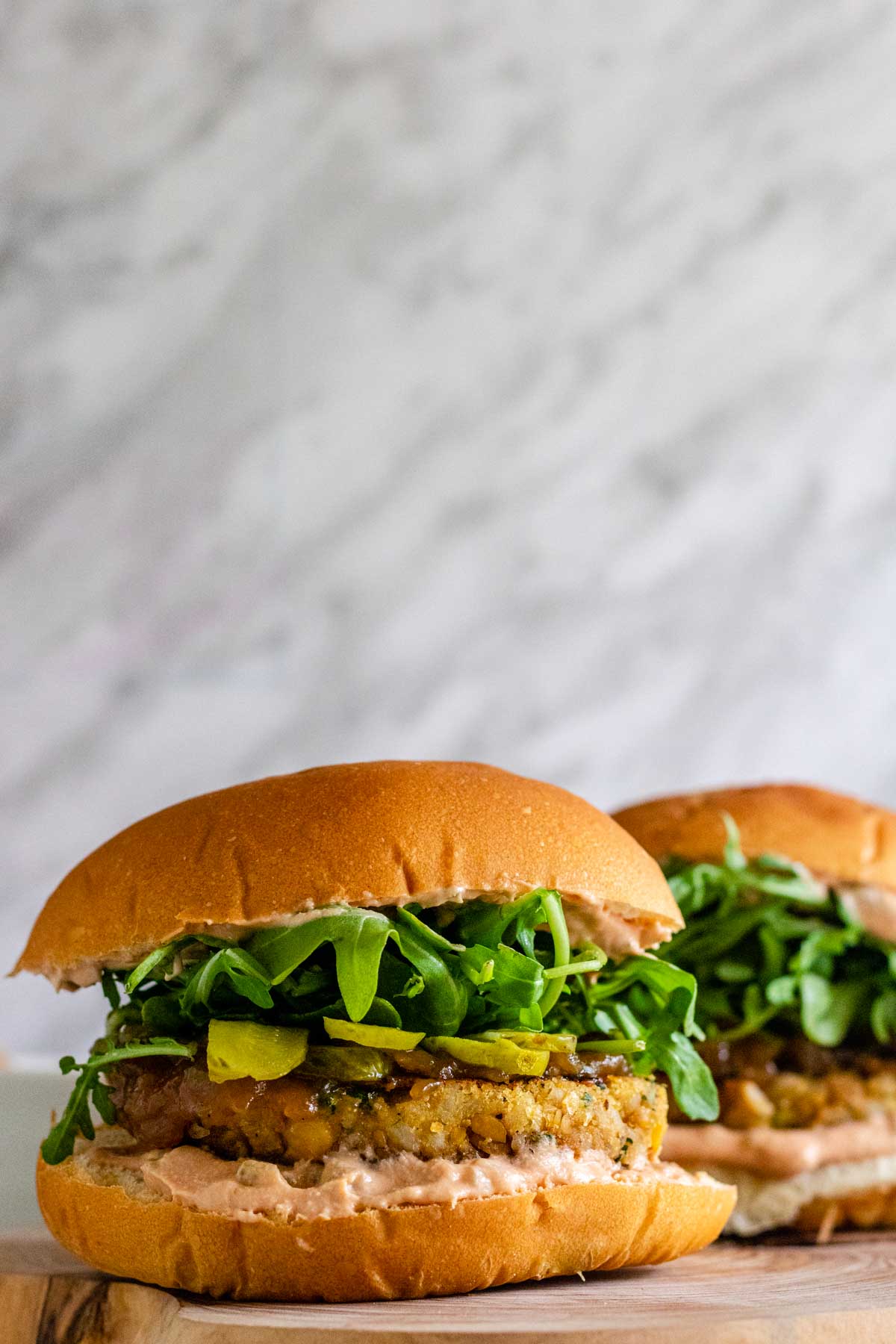 Chickpea burgers on buns with sauce, pickles, and arugula.