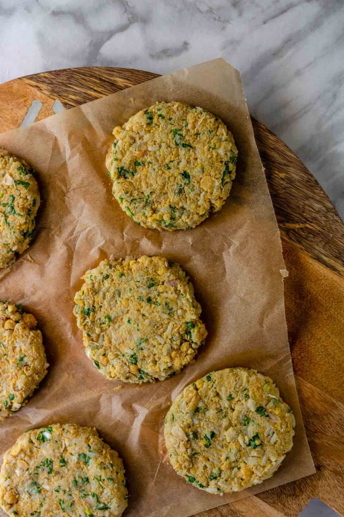 Formed chickpea patties sit on a parchment paper line wooden board.