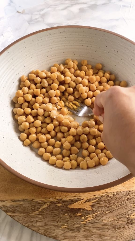 A hand mashes chickpeas with a fork.