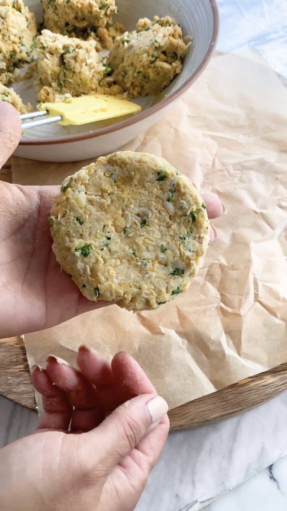 A hand holds a flat formed chickpea patty.