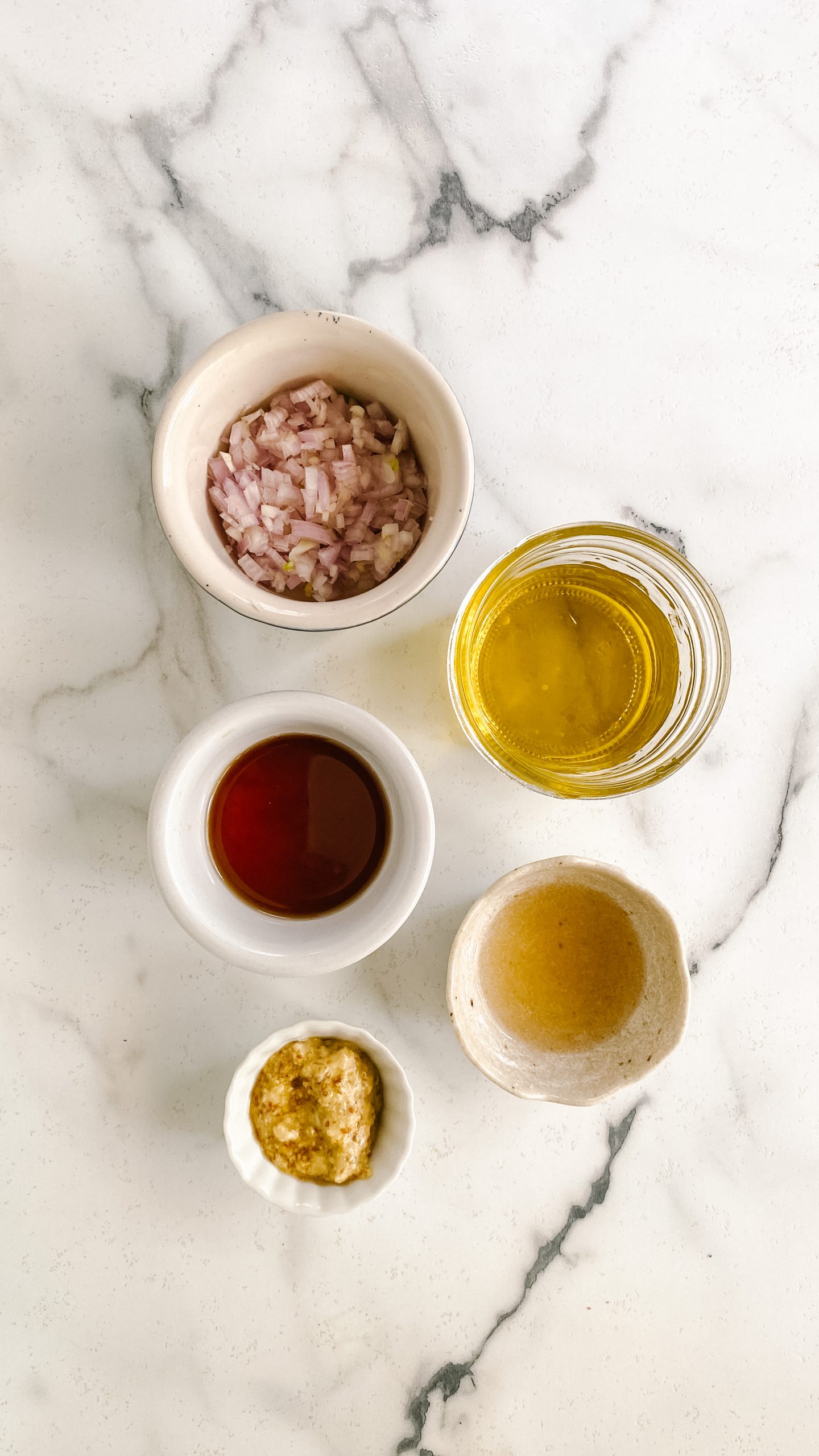 Dressing ingredients in small bowls on a white marble counter.