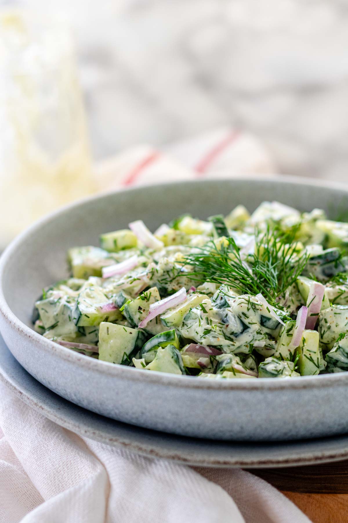 Chopped cucumbers in a bowl covered in tzatziki sauce, garnished with fresh dill.