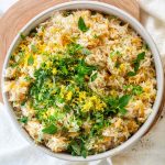 Rice in a bowl topped with lemon zest and fresh herbs.