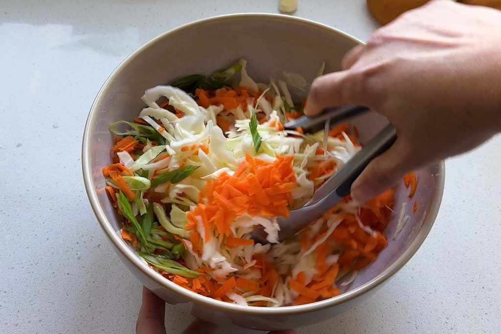 Cabbage and carrots being mixed with tongs.