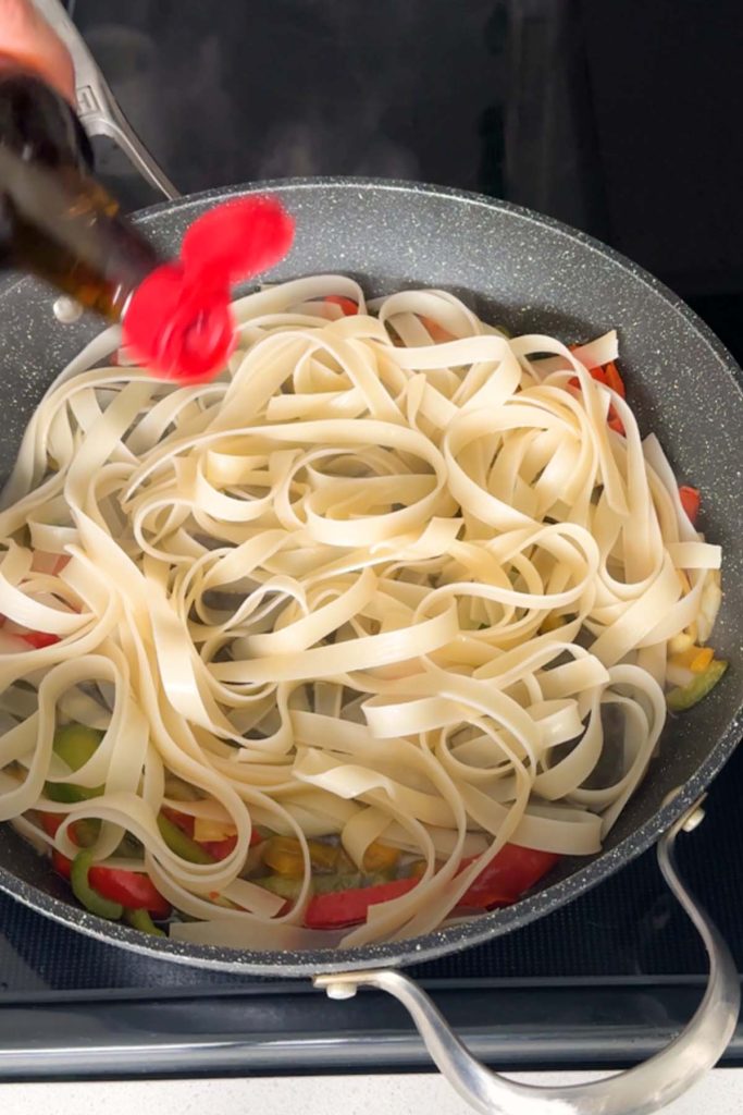 Noodles sauteing in a pan with peppers.
