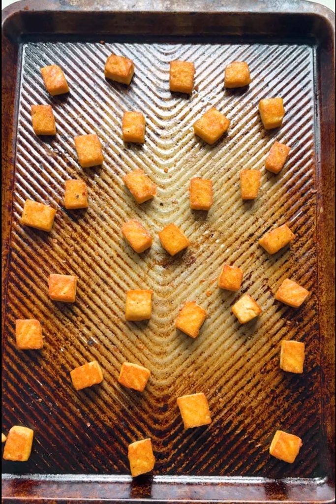 Golden baked tofu cubes on a baking sheet ready for peanut noodle bowls