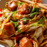 Spicy Peanut Tofu Bowl with rice noodles, red peppers, and creamy peanut sauce with chopsticks.