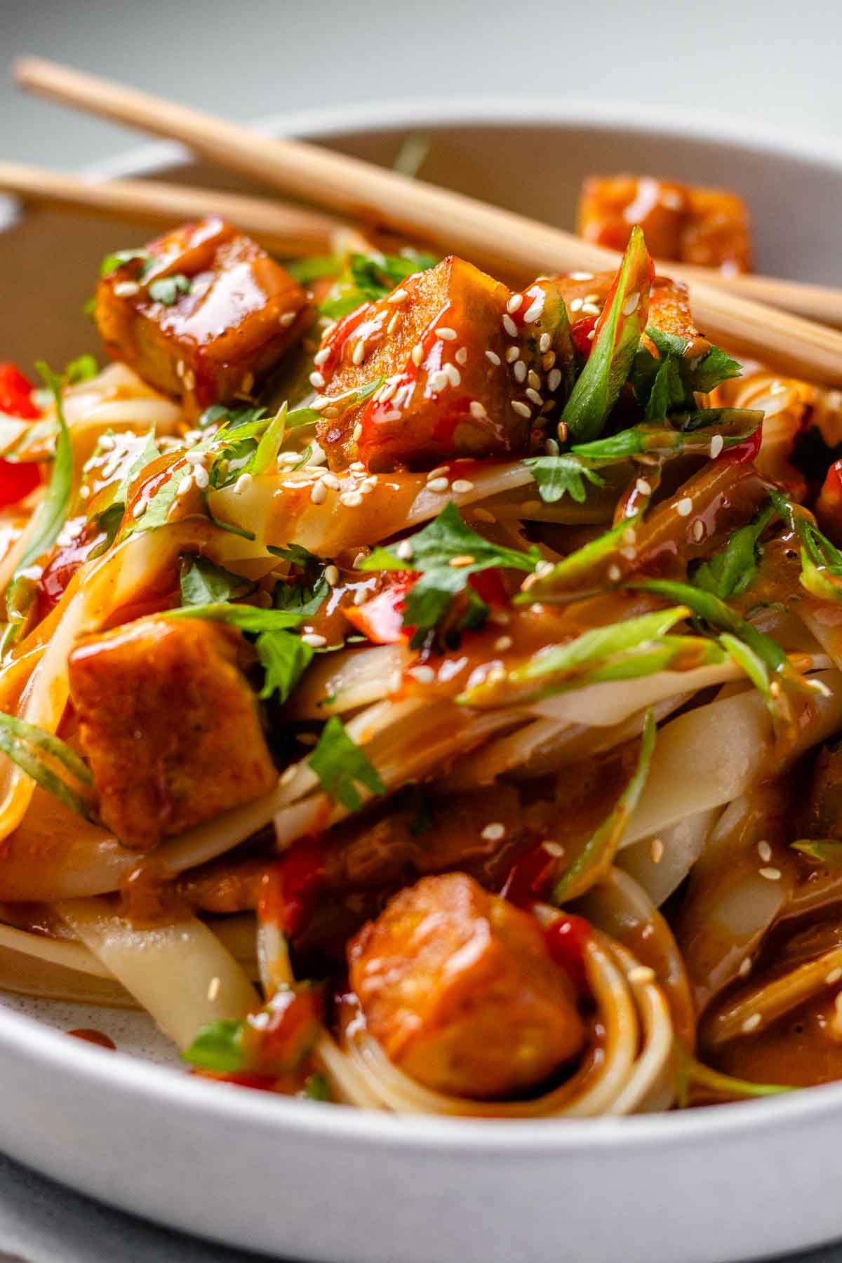 Spicy Peanut Tofu Bowl with rice noodles, red peppers, and creamy peanut sauce with chopsticks.