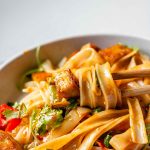 Spicy Peanut Tofu Bowl with rice noodles, red peppers, and creamy peanut sauce with chopsticks.