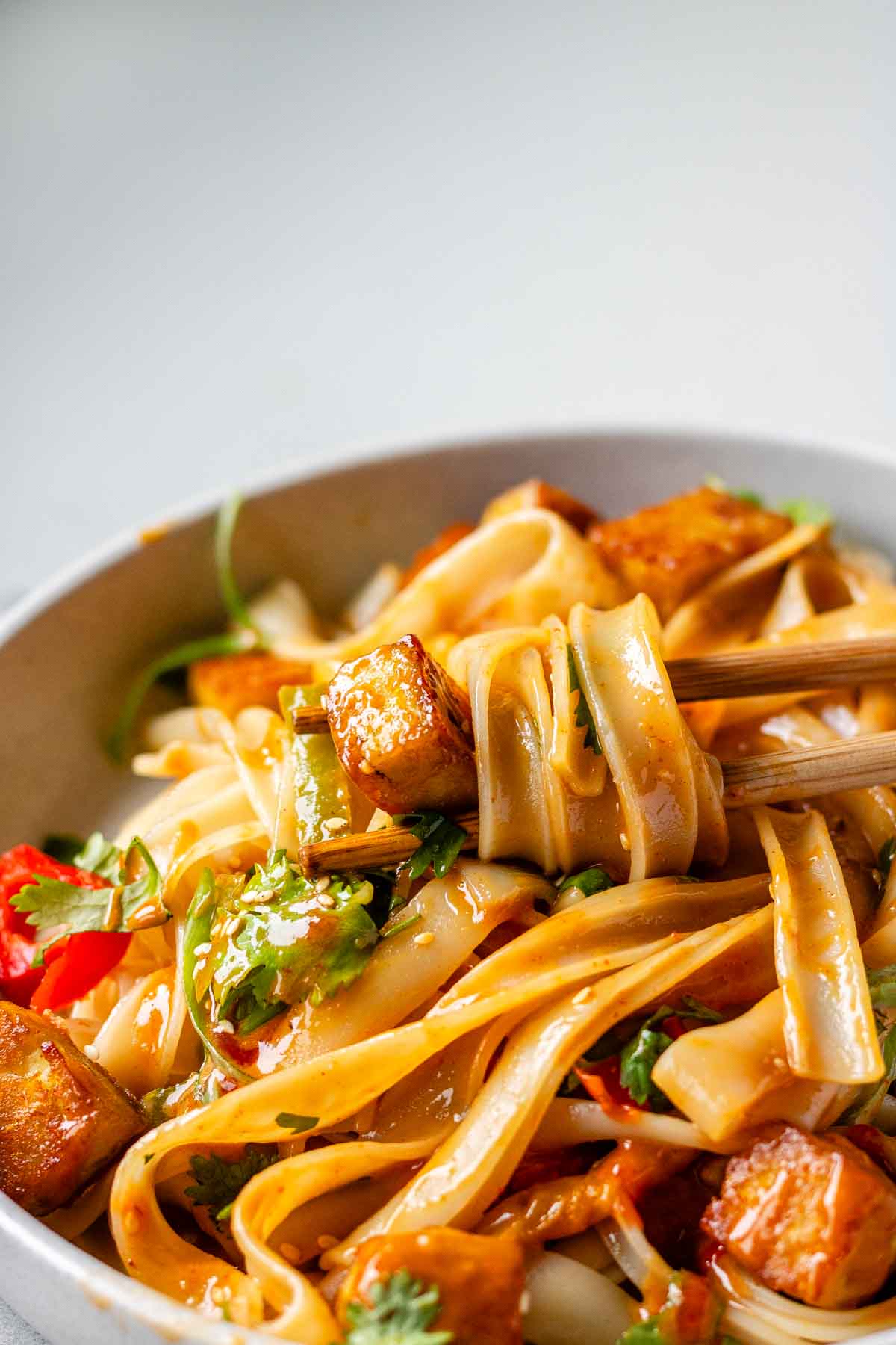 Spicy Peanut Tofu Bowl with rice noodles, red peppers, and creamy peanut sauce with chopsticks.