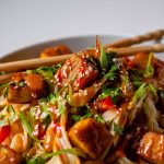 Spicy Peanut Tofu Bowl with rice noodles, red peppers, and creamy peanut sauce with chopsticks.
