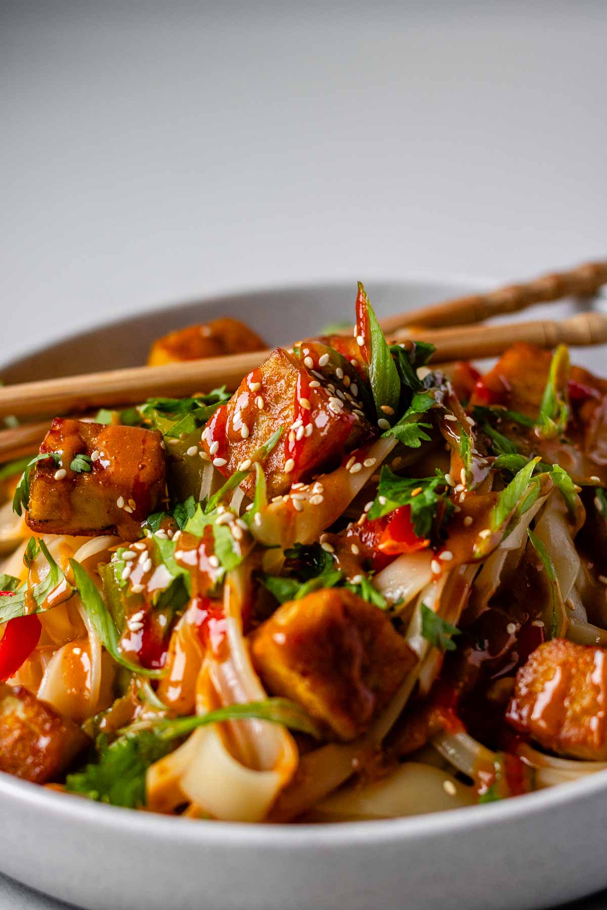 Spicy Peanut Tofu Bowl with rice noodles, red peppers, and creamy peanut sauce with chopsticks.