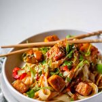 Spicy Peanut Tofu Bowl with rice noodles, red peppers, and creamy peanut sauce with chopsticks.