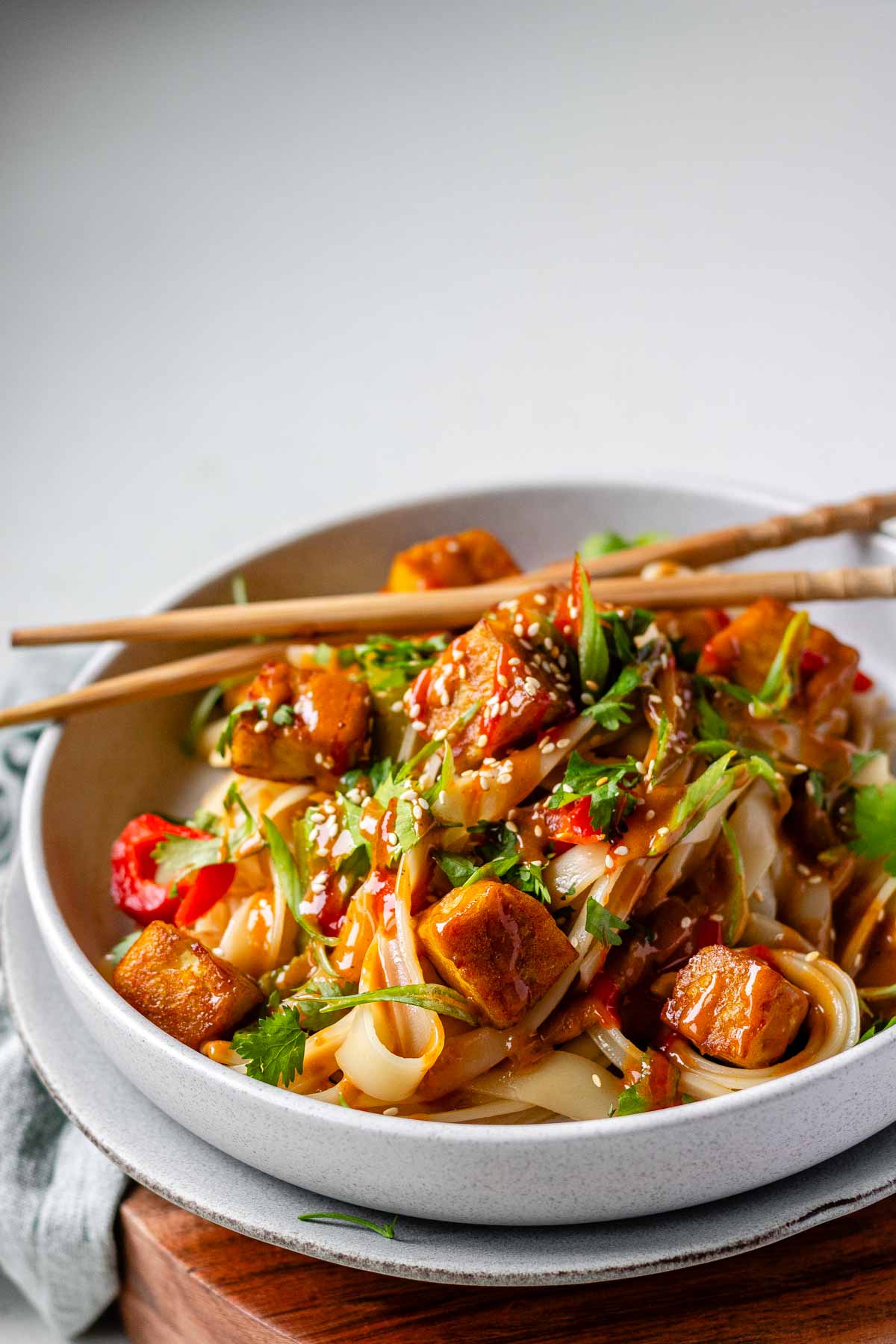 Spicy Peanut Tofu Bowl with rice noodles, red peppers, and creamy peanut sauce with chopsticks.
