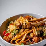 Spicy Peanut Tofu Bowl with rice noodles, red peppers, and creamy peanut sauce with chopsticks with the text peanut noodle bowls.