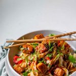 Spicy Peanut Tofu Bowl with rice noodles, red peppers, and creamy peanut sauce with chopsticks with the text spicy peanut noodle bowls.
