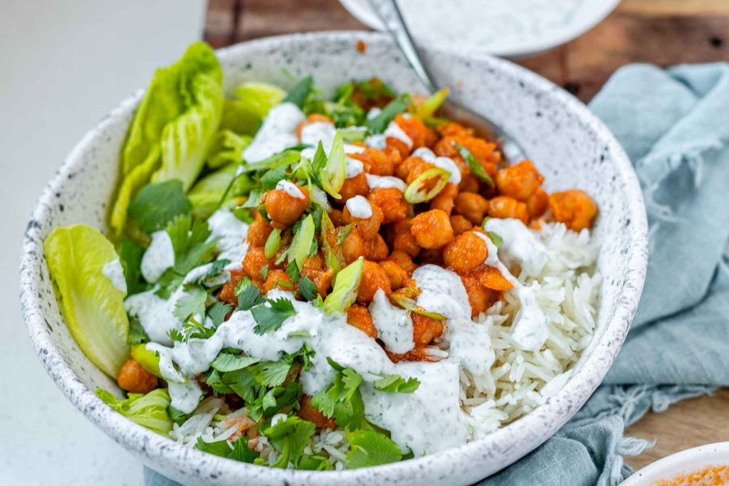A bowl with rice, chickpeas, salad and a white sauce.