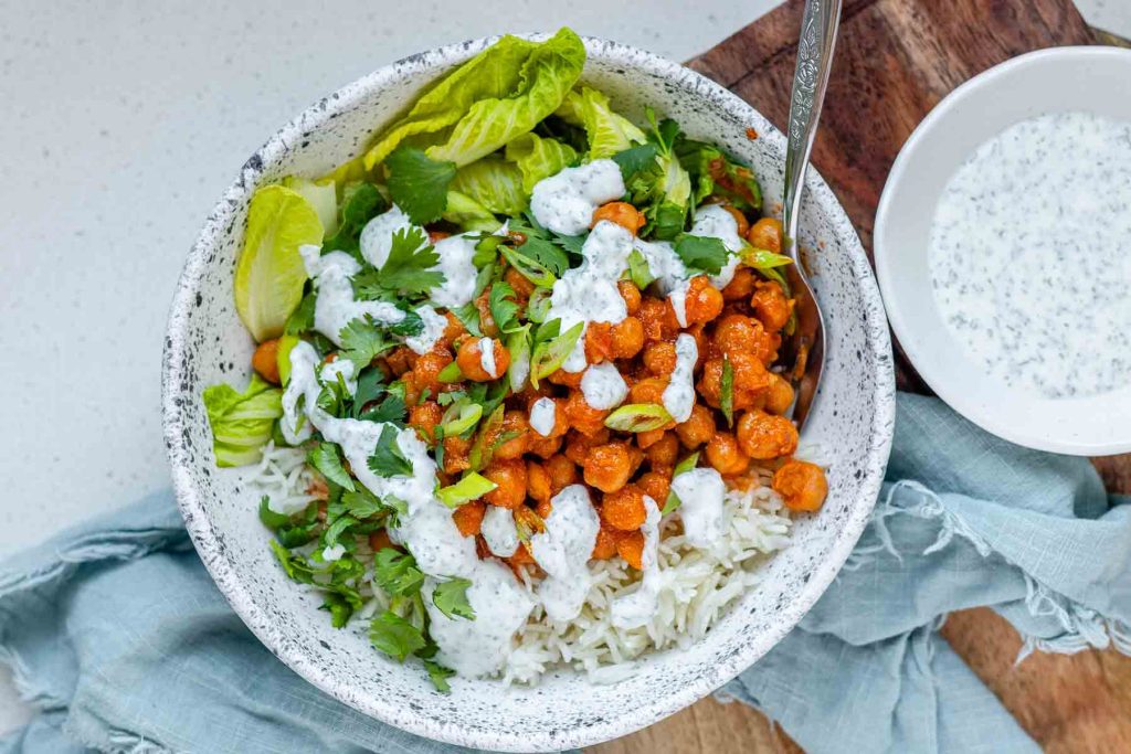 A bowl with rice, chickpeas, salad and a white sauce.