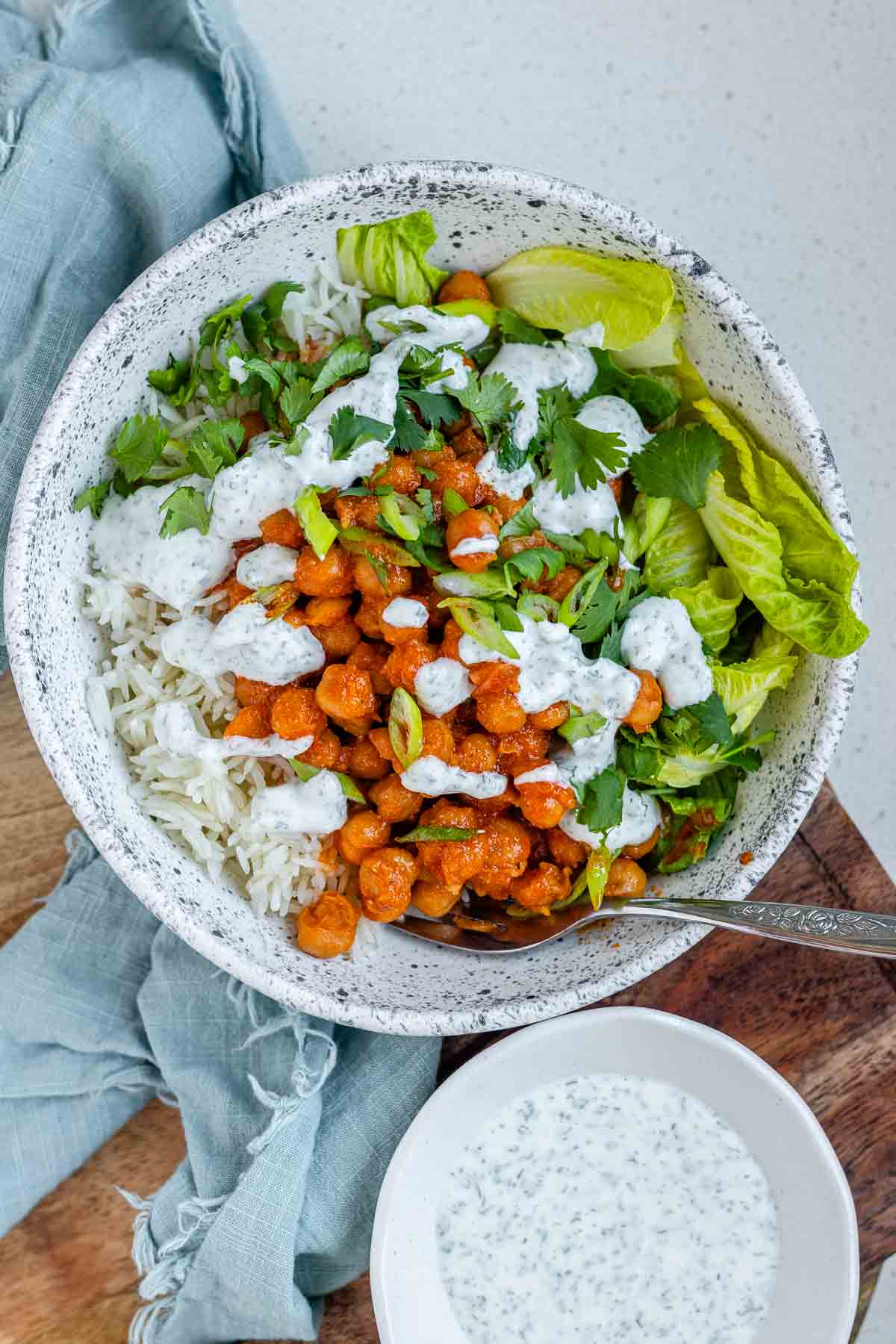 A bowl with rice, chickpeas, salad and a white sauce.