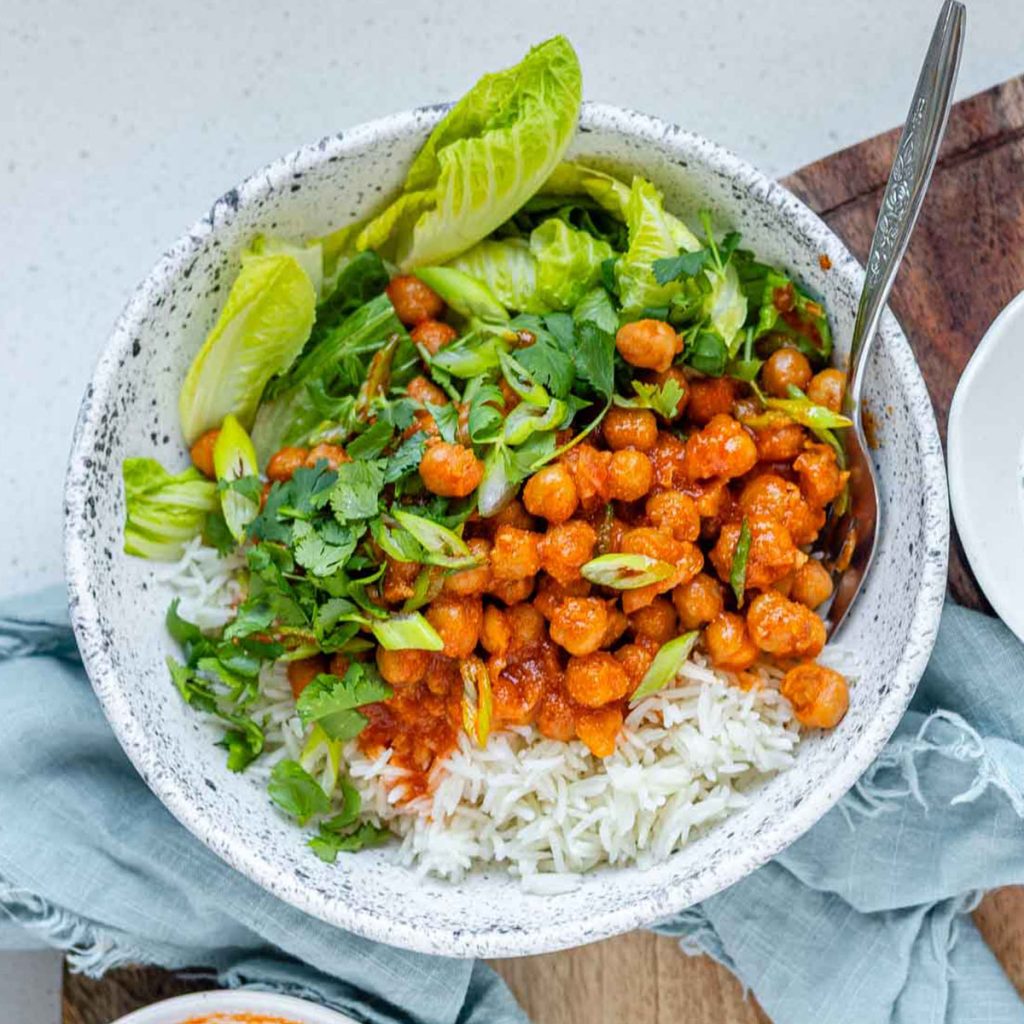 A bowl with rice, chickpeas, salad and a white sauce.