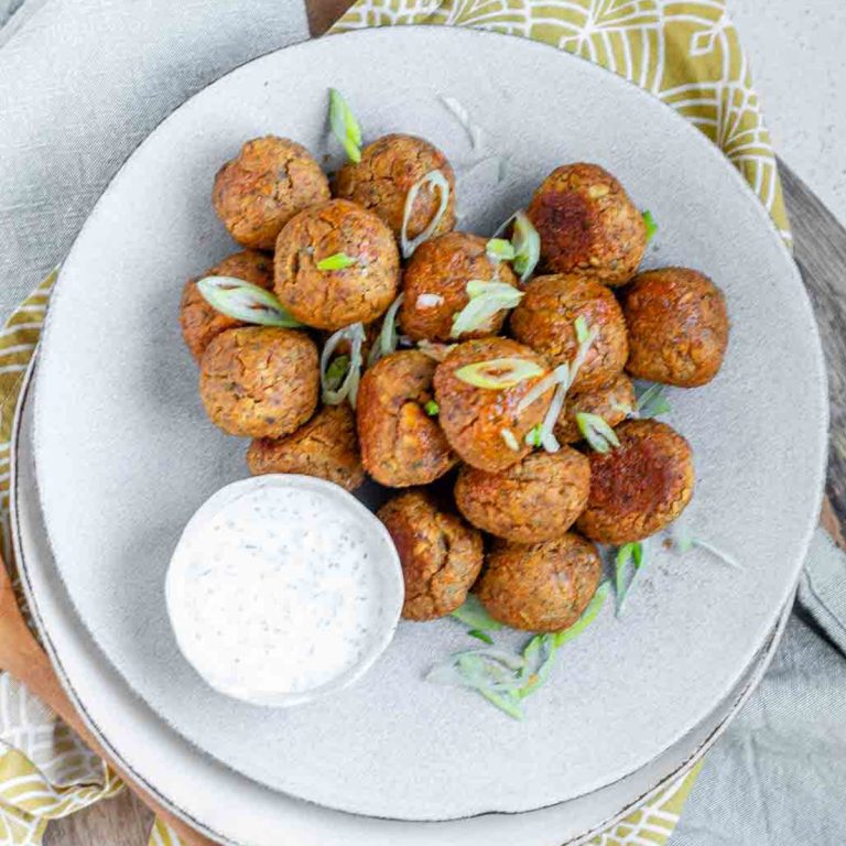 Veggie balls on a plate with a bowl of white sauce.