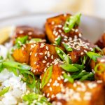Tofu in sauce in a bowl beside rice, garnished with lemon slices and green onions.