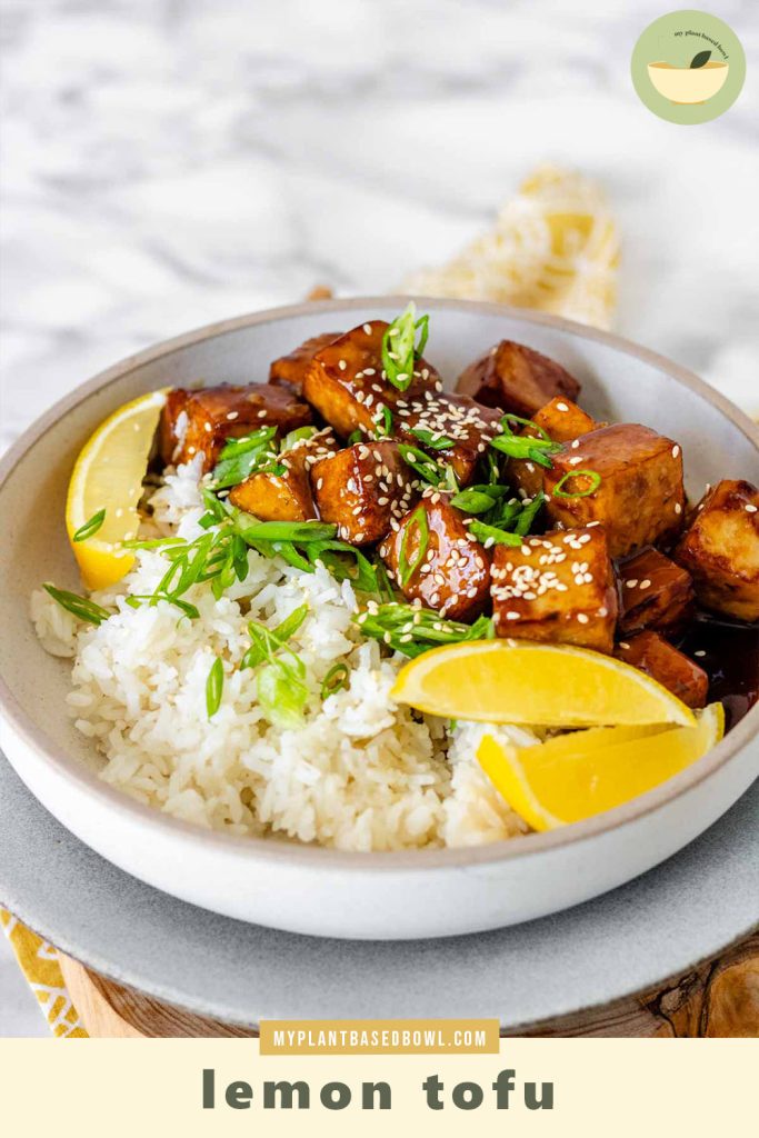 Tofu in sauce in a bowl beside rice, garnished with lemon slices and green onions with the text lemon tofu.