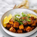 Tofu in sauce in a bowl beside rice, garnished with lemon slices and green onions with the text lemon tofu.