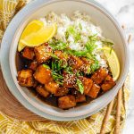 Tofu in sauce in a bowl beside rice, garnished with lemon slices and green onions with the text lemon tofu.