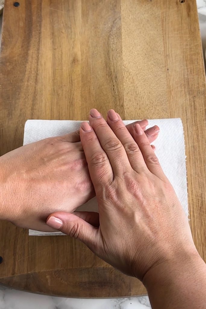 Hands pressing tofu between paper towels.