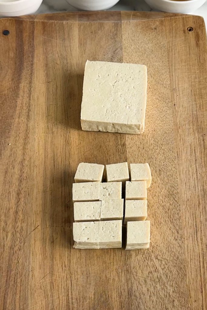 Tofu cut into squares on a cutting board.