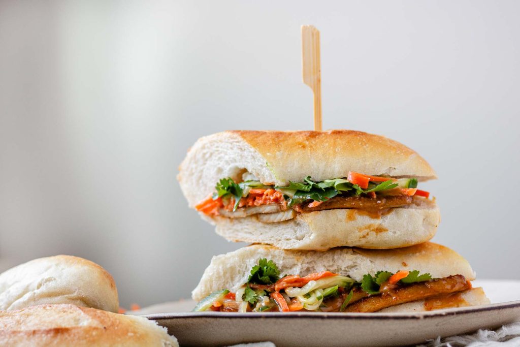 A halved, stacked sandwich with vegetables, tofu, and peanut sauce.