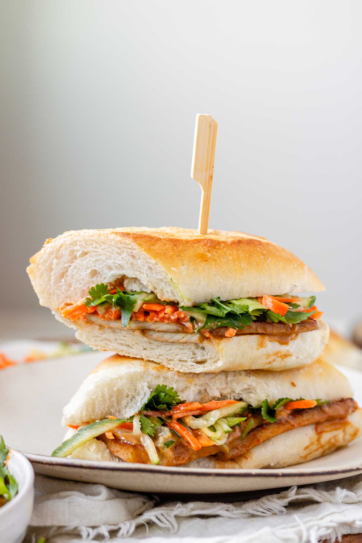 A halved, stacked sandwich with vegetables, tofu, and peanut sauce.