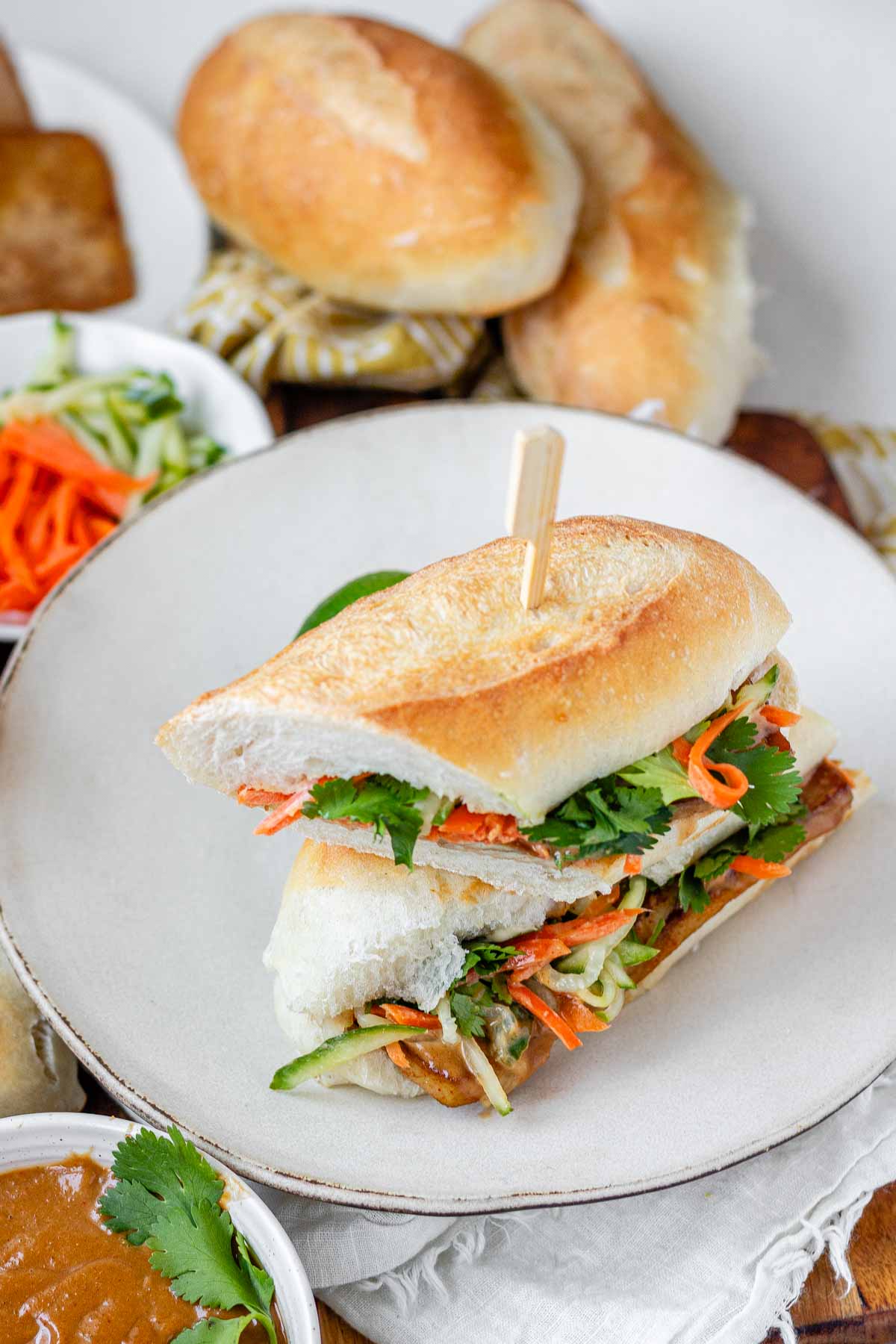 A halved, stacked sandwich with vegetables, tofu, and peanut sauce.