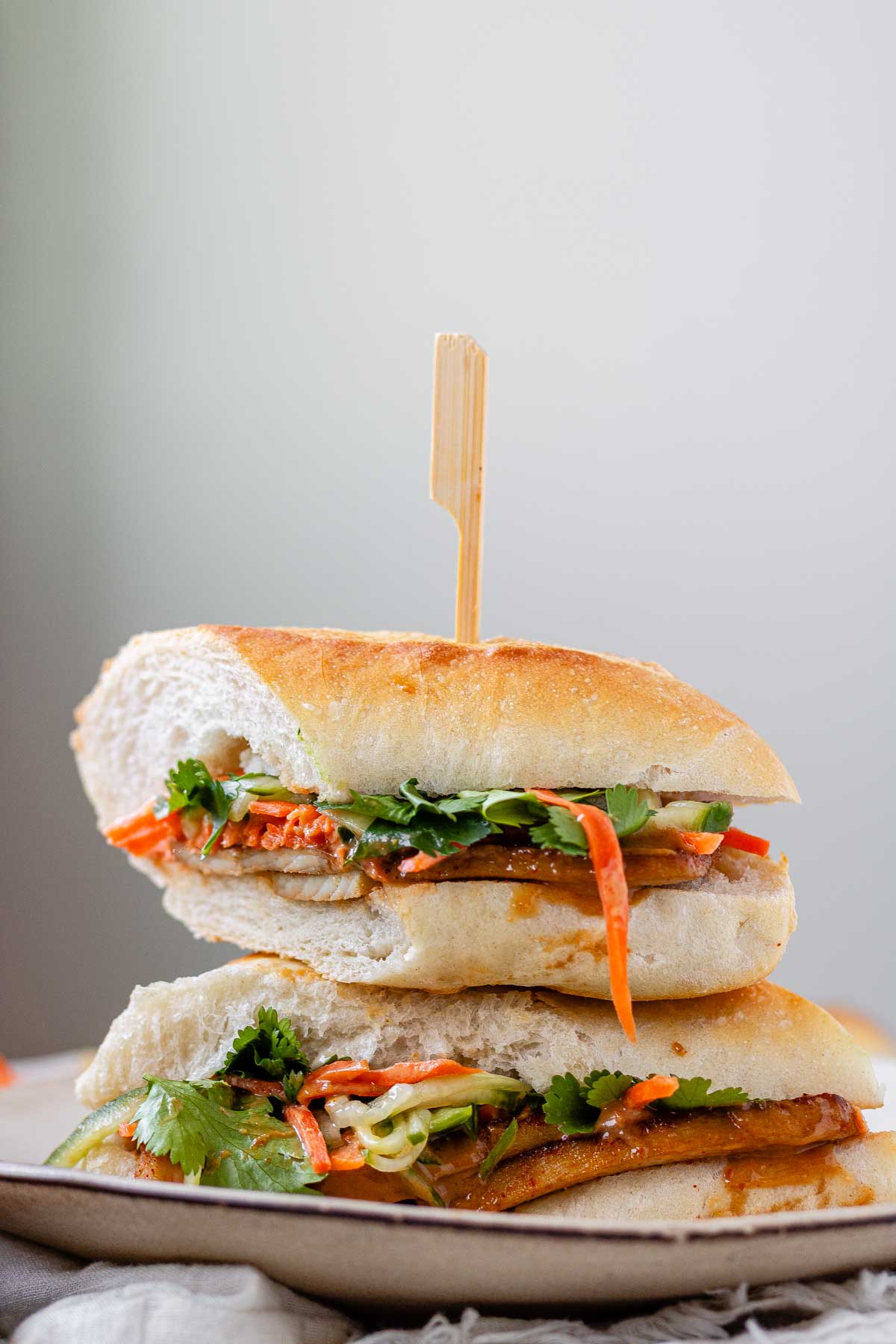 A halved, stacked sandwich with vegetables, tofu, and peanut sauce.
