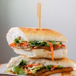 A halved, stacked sandwich with vegetables, tofu, and peanut sauce with the textu tofu banh mi.