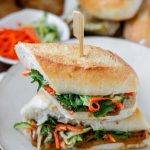A halved, stacked sandwich with vegetables, tofu, and peanut sauce with the textu tofu banh mi.