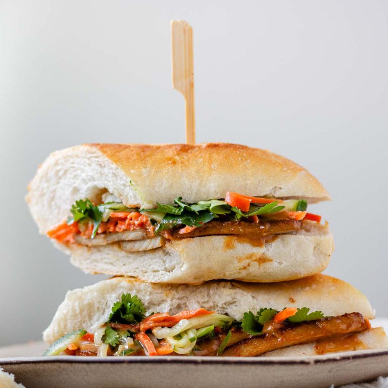A halved, stacked sandwich with vegetables, tofu, and peanut sauce.