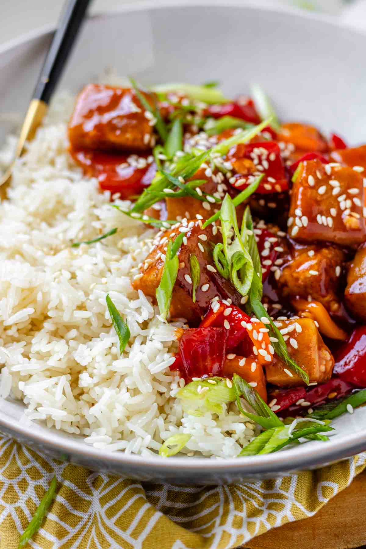 Tofu in sauce in a bowl beside rice, garnished with green onions.