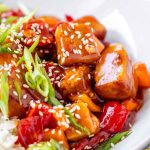 Tofu in sauce in a bowl beside rice, garnished with green onions.
