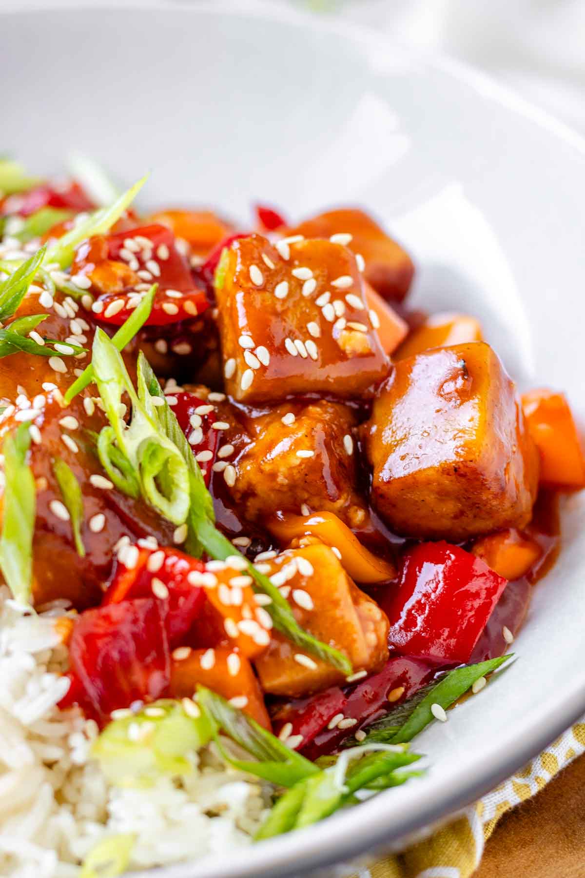 Tofu in sauce in a bowl beside rice, garnished with green onions.