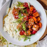 Tofu in sauce in a bowl beside rice, garnished with green onions.